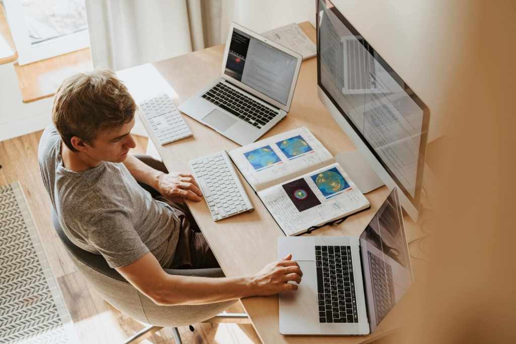 カジュアルな服装の男性が3台のコンピュータを使用して在宅勤務中