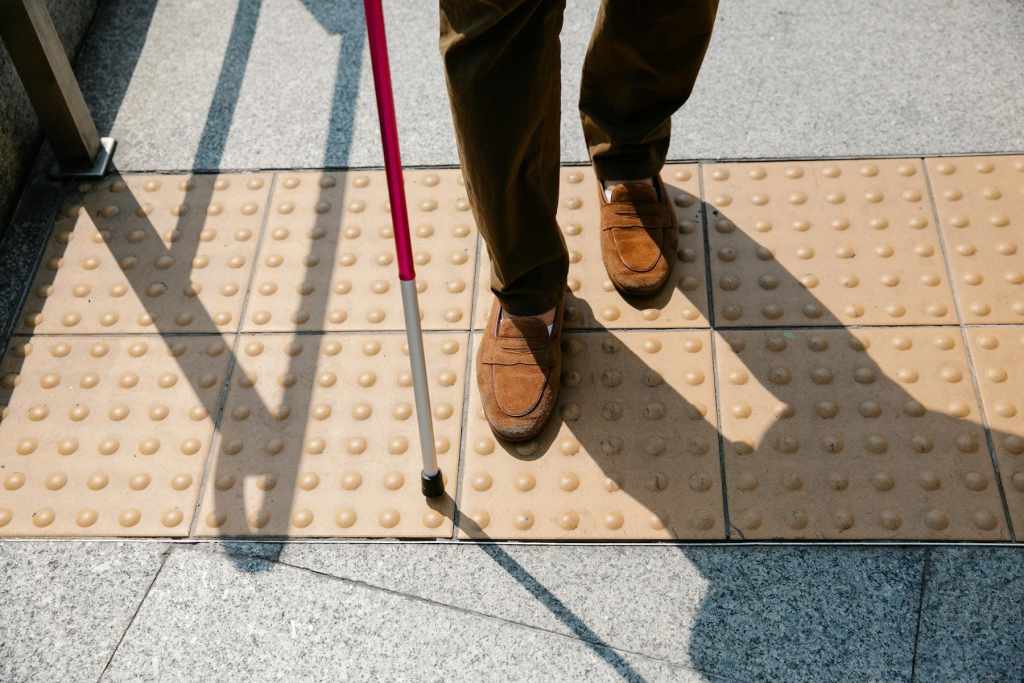 茶色の靴を履いた人物が、白杖を持って点字ブロックの上を歩いている