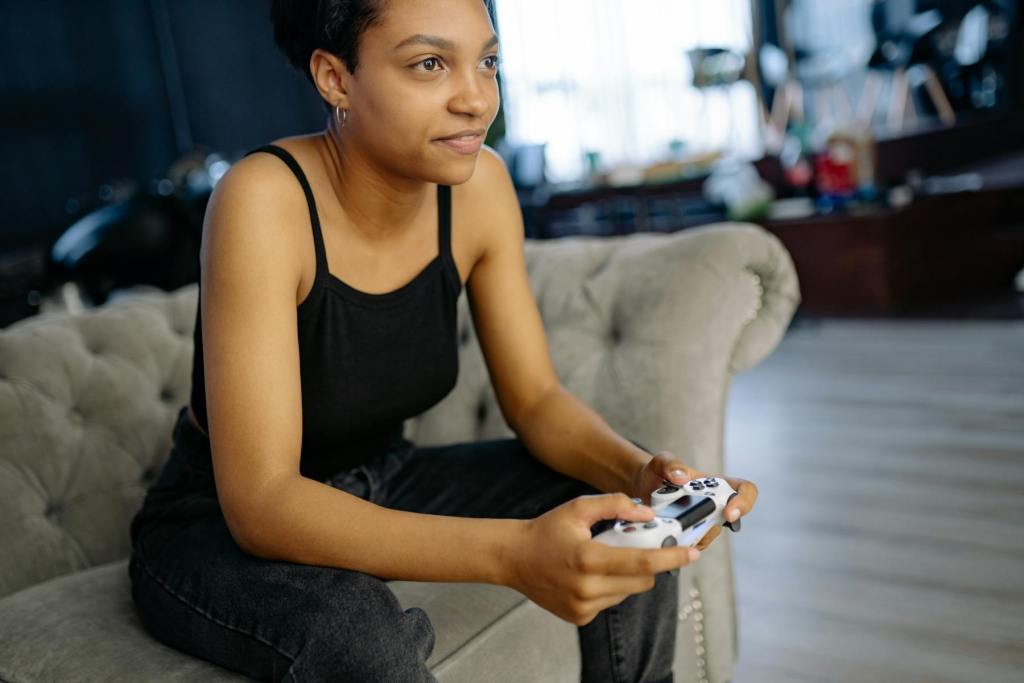 ソファでコンソールゲームを遊ぶ若い女性