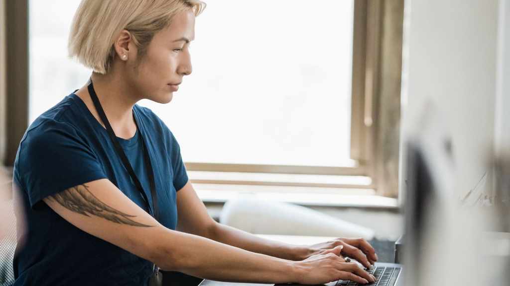 半袖シャツを着て上腕に大きなタトゥーのある人物が、オフィスでパソコン作業をしている様子